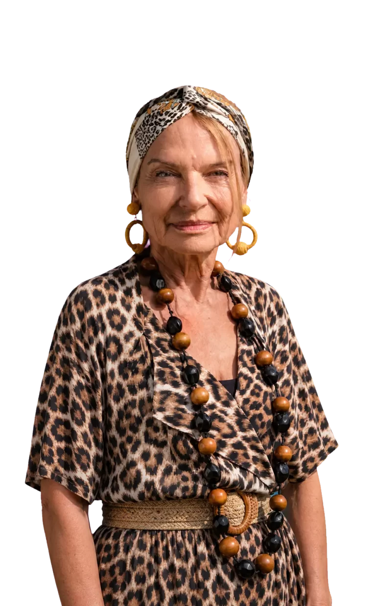 Portrait of an older woman wearing a leopard print dress and matching headscarf, with large brown and black beaded necklace and yellow earrings.