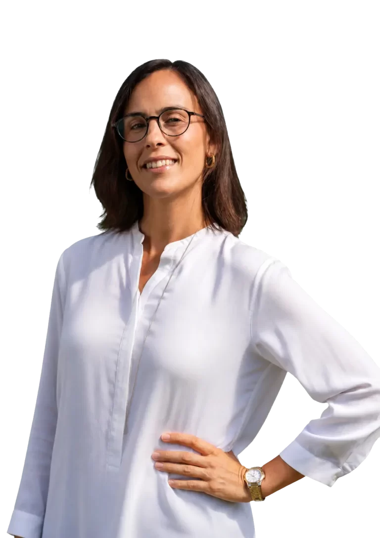Woman with shoulder-length brown hair, glasses, and gold hoop earrings posing in a white blouse, smiling with hand on hip.