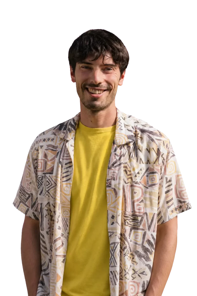 Smiling man in a yellow shirt and patterned short-sleeve shirt, standing against a black background with pink lines.